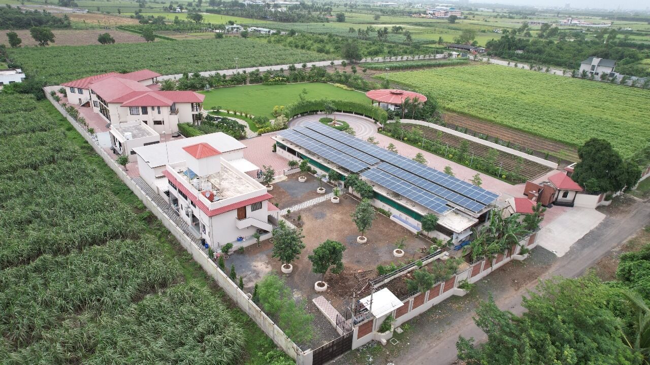 Aerial view of solar carport panels in the courtyard of a Green Lab Farm House compound surrounded by fields