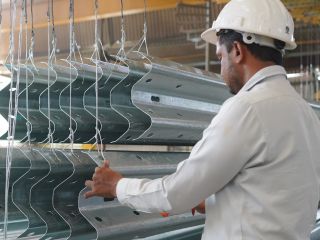 Technician in white helmet examining galvanized crash-barrier beams
