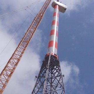 A tall, galvanized steel windmill lattice tower designed to support a large wind turbine for renewable energy generation.