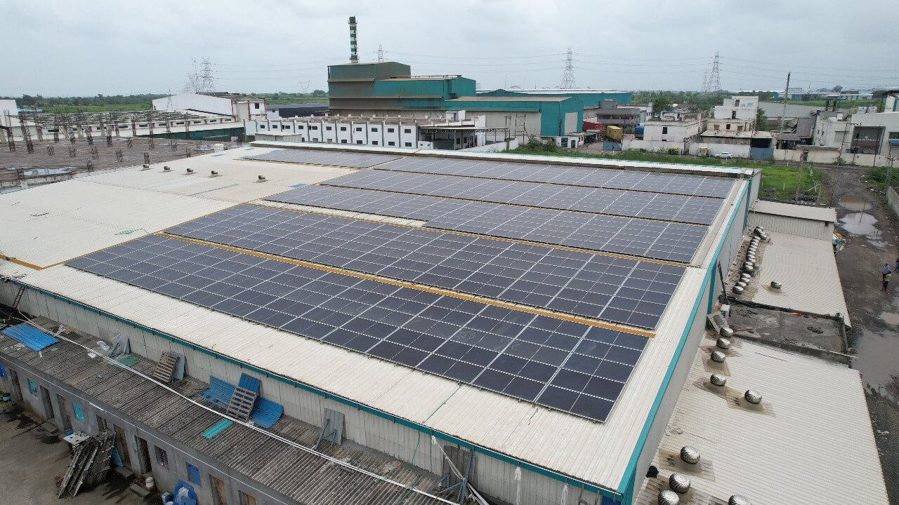 Aerial view of solar panel arrays on a Nipun industrial roof with surrounding factory buildings