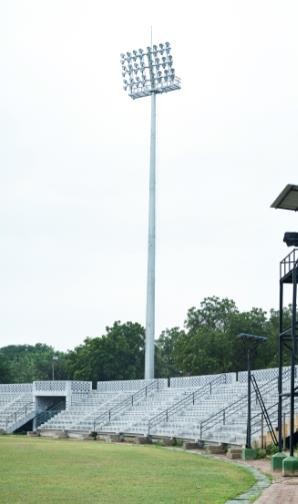 A high-mast lighting tower with multiple lamps, illuminating a large industrial area at night.